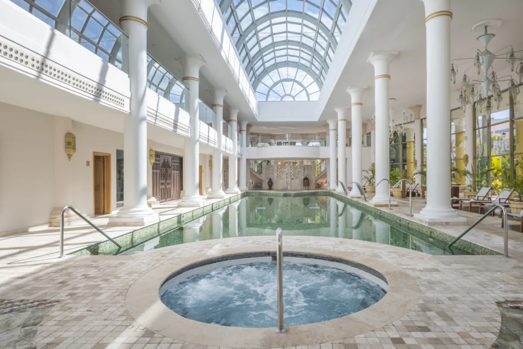 Interior del centro de bienestar con piscina rodeada de columnas blancas e iluminación natural en JOIA Paraíso.