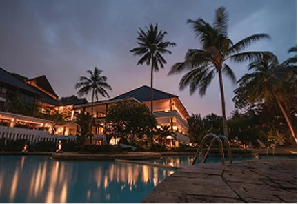 Vista nocturna de la piscina iluminada y la arquitectura tropical de Caribbean Suites en Islas Caimán bajo un cielo al atardecer