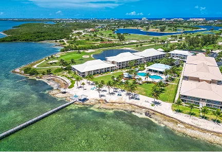 Vista aérea panorámica del Holiday Inn Resort Grand Cayman, mostrando sus edificios frente al mar, muelle privado, piscina exterior y amplias zonas verdes junto a una laguna cristalina.