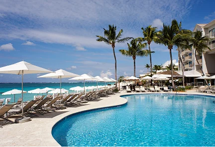 Piscina infinita de forma curva rodeada de sombrillas blancas y camastros frente al mar en el Marriott Grand Cayman Resort.