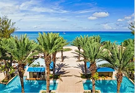 Vista simétrica de las piscinas de lujo y jardines con palmeras de The Ritz-Carlton, Grand Cayman, con el mar Caribe de fondo.