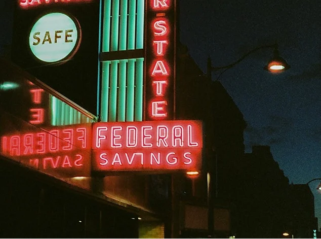 Imagen de carteles de neón vintage de color rojo neón con las palabras 'FEDERAL SAVINGS' y 'SAFE' encendidas de noche, utilizada para ilustrar la card del tour de fantasmas y misterios paranormales en Dallas. Esta excursión explora el lado más oscuro e histórico de la ciudad mundialista.